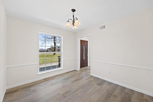 spare room with baseboards, wood finished floors, visible vents, and a notable chandelier