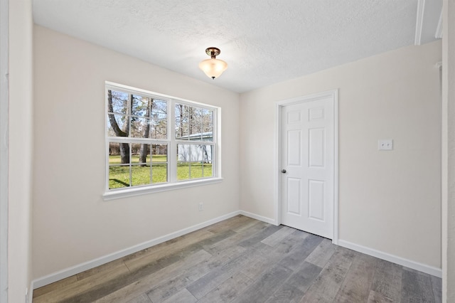 unfurnished room featuring a textured ceiling, baseboards, and wood finished floors