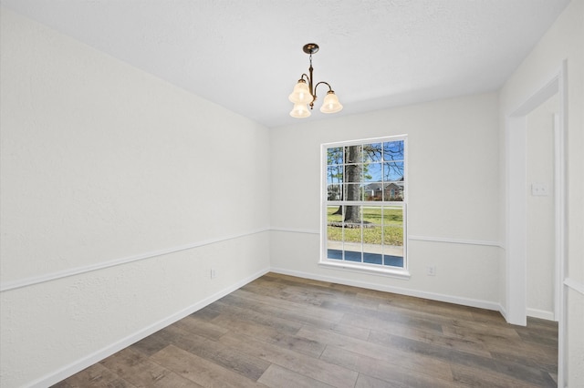 empty room with a notable chandelier, baseboards, and wood finished floors