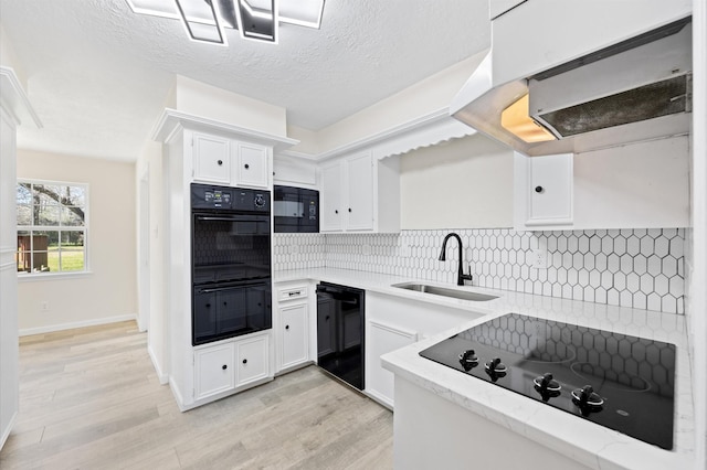 kitchen with tasteful backsplash, white cabinetry, a sink, under cabinet range hood, and black appliances