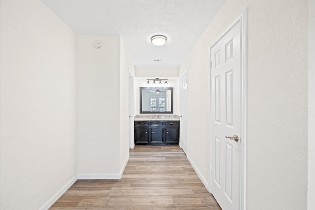 corridor with light wood-style flooring, baseboards, and a textured ceiling