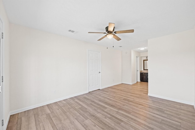 spare room with light wood-style flooring, a ceiling fan, visible vents, and baseboards