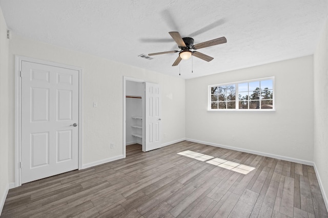 unfurnished bedroom with baseboards, a ceiling fan, wood finished floors, a walk in closet, and a textured ceiling