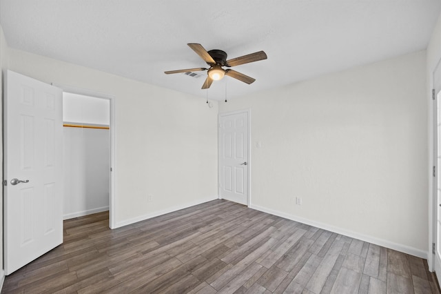 unfurnished bedroom with baseboards, visible vents, wood finished floors, a spacious closet, and a closet