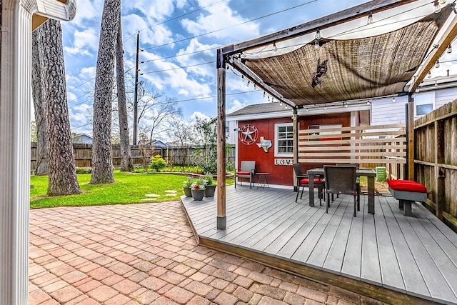 wooden terrace featuring outdoor dining space, a patio area, a fenced backyard, and a lawn