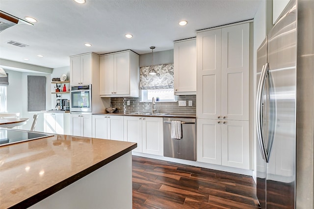 kitchen featuring dark wood finished floors, stainless steel appliances, white cabinets, pendant lighting, and backsplash