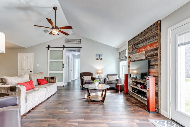 living area featuring visible vents, dark wood-type flooring, a barn door, ceiling fan, and vaulted ceiling