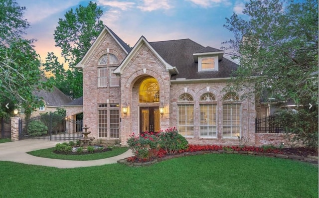 view of front of house featuring brick siding, concrete driveway, a front yard, french doors, and a gate