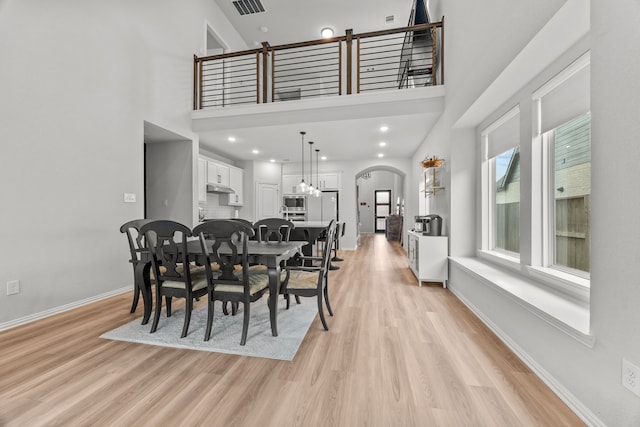 dining area with arched walkways, light wood-style flooring, visible vents, a towering ceiling, and baseboards