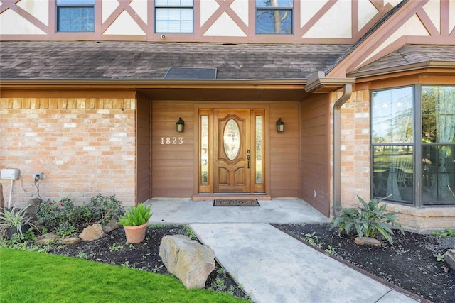 view of exterior entry with a shingled roof and brick siding