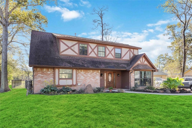 tudor house with brick siding, a front yard, a shingled roof, and stucco siding