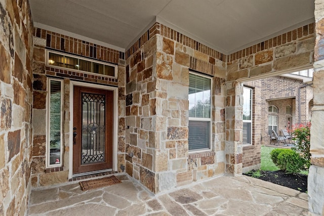 view of exterior entry with stone siding, a porch, and brick siding