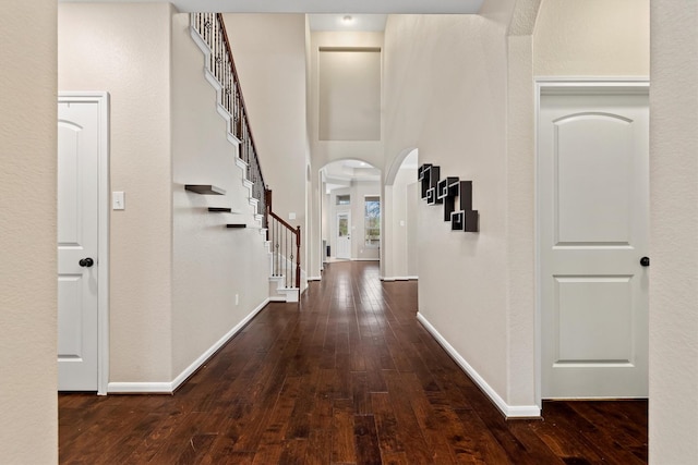 hall featuring stairway, baseboards, arched walkways, and dark wood finished floors