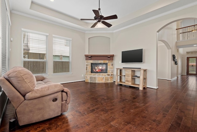 living room featuring a tray ceiling, wood-type flooring, a stone fireplace, and baseboards