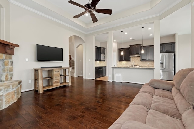 living area featuring ceiling fan, a tray ceiling, dark wood finished floors, and ornamental molding