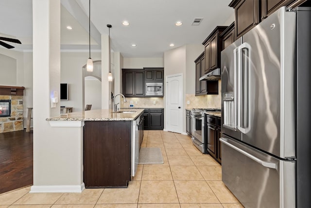 kitchen with light tile patterned floors, stainless steel appliances, a sink, dark brown cabinetry, and under cabinet range hood