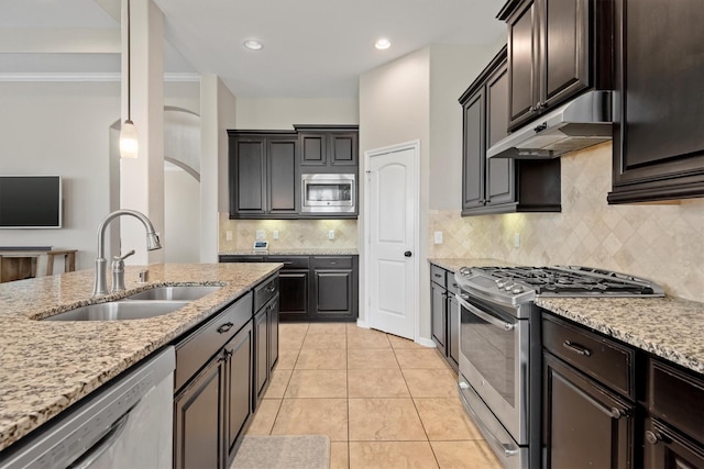 kitchen featuring light tile patterned floors, appliances with stainless steel finishes, light stone counters, under cabinet range hood, and a sink