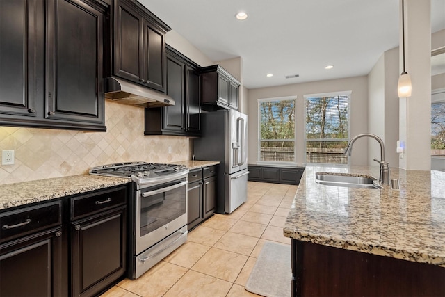 kitchen with light stone countertops, under cabinet range hood, appliances with stainless steel finishes, and a sink