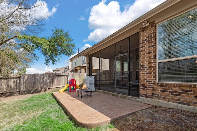 view of yard featuring a sunroom, a patio area, fence, and a fire pit