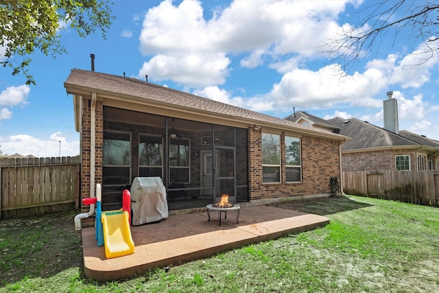 back of house with an outdoor fire pit, a sunroom, a fenced backyard, and a lawn