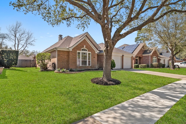 view of front of house featuring an attached garage, brick siding, concrete driveway, a front lawn, and a chimney