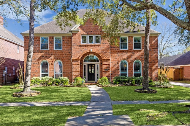 view of front of home with a front lawn, fence, brick siding, and roof with shingles