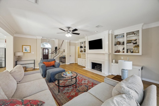 living area with visible vents, light wood finished floors, a fireplace, stairs, and crown molding