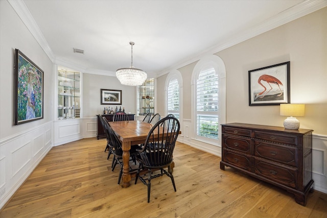 dining room featuring crown molding, a decorative wall, visible vents, and light wood finished floors