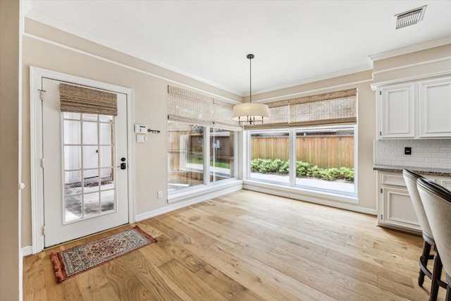 unfurnished dining area with ornamental molding, visible vents, light wood-style flooring, and baseboards