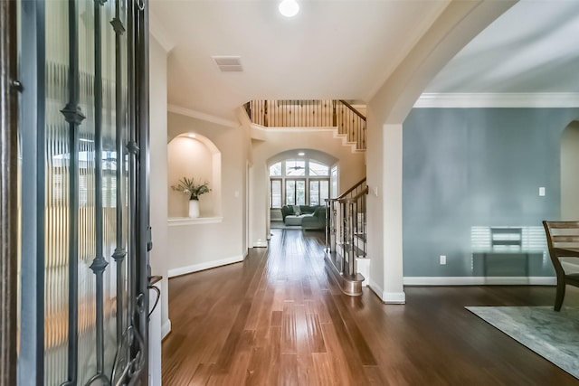 entryway featuring arched walkways, wood finished floors, stairs, and crown molding