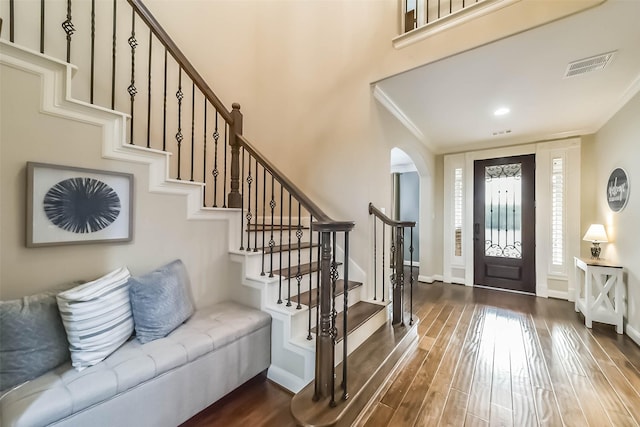 foyer entrance featuring arched walkways, wood finished floors, visible vents, baseboards, and ornamental molding