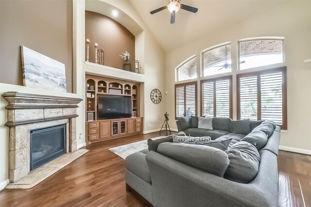 living area with ceiling fan, a fireplace, high vaulted ceiling, and wood finished floors