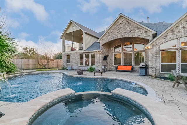 rear view of property with a balcony, ceiling fan, fence, a patio area, and brick siding