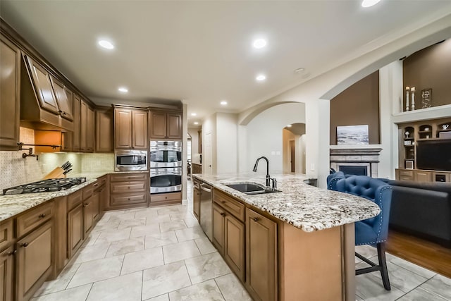 kitchen with arched walkways, a breakfast bar area, a sink, appliances with stainless steel finishes, and light stone countertops