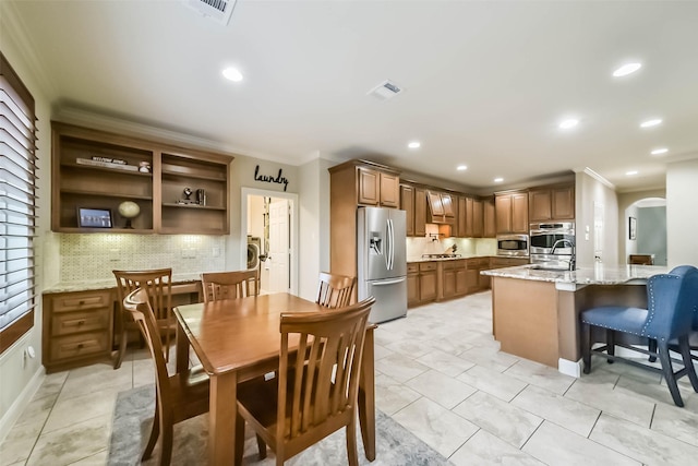 kitchen featuring arched walkways, stainless steel appliances, decorative backsplash, ornamental molding, and a sink