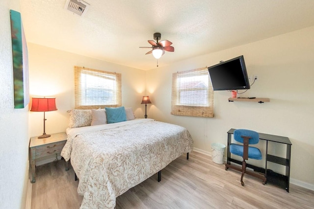 bedroom with multiple windows, visible vents, a textured ceiling, and wood finished floors