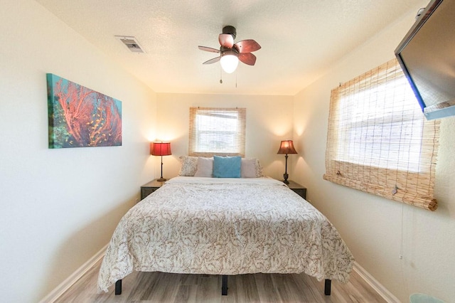 bedroom featuring a ceiling fan, visible vents, baseboards, and wood finished floors