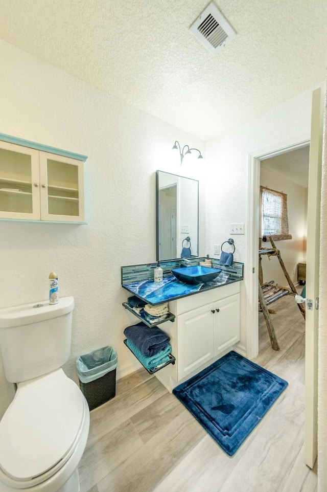 bathroom with toilet, a textured ceiling, wood finished floors, and visible vents