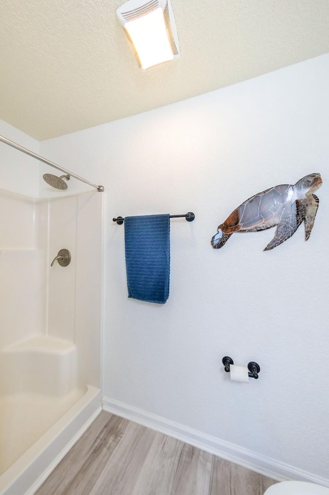 bathroom with walk in shower, a textured ceiling, baseboards, and wood finished floors