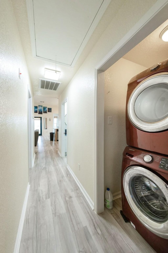 hall featuring visible vents, light wood-style flooring, attic access, stacked washer / dryer, and baseboards