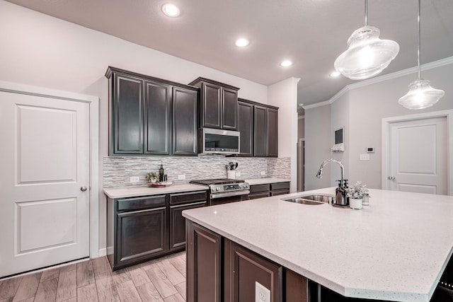 kitchen with decorative light fixtures, stainless steel appliances, backsplash, a sink, and an island with sink