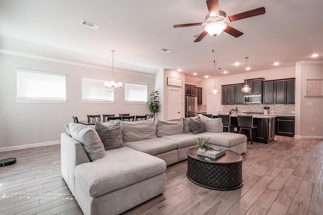 living area featuring baseboards, visible vents, light wood finished floors, and ceiling fan with notable chandelier