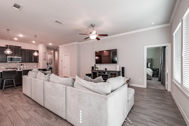 living area with baseboards, visible vents, wood finished floors, and ornamental molding