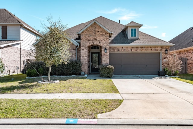 french provincial home with a garage, brick siding, a shingled roof, concrete driveway, and a front yard