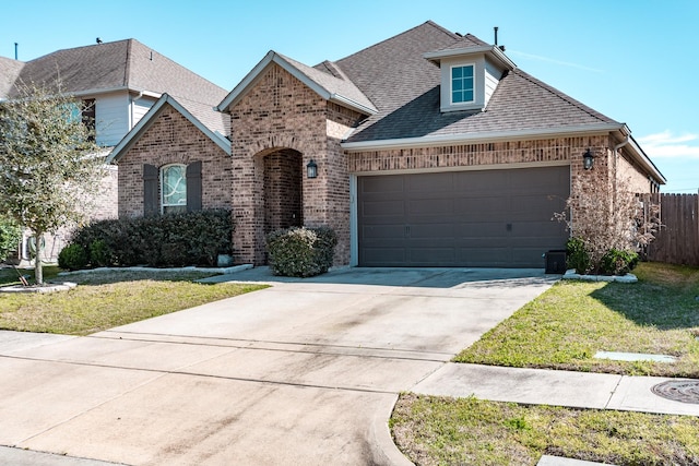 french provincial home with a garage, concrete driveway, brick siding, and a front yard