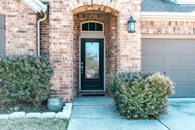 property entrance featuring brick siding, an attached garage, and roof with shingles