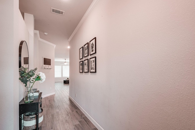 hall with baseboards, wood finished floors, visible vents, and crown molding