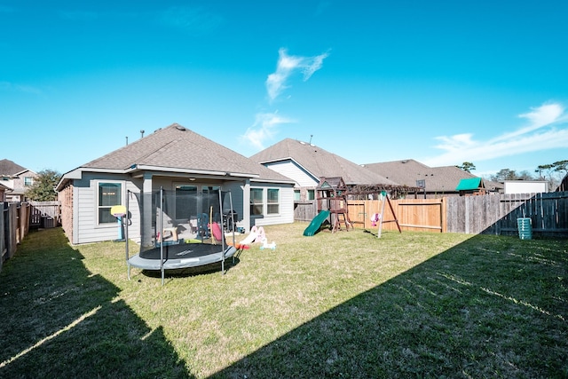 rear view of house with a yard, a trampoline, a playground, and a fenced backyard