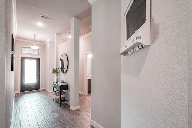 entryway with wood finish floors, crown molding, visible vents, a textured wall, and baseboards