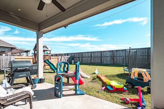 view of play area with a trampoline, a fenced backyard, a lawn, and a ceiling fan